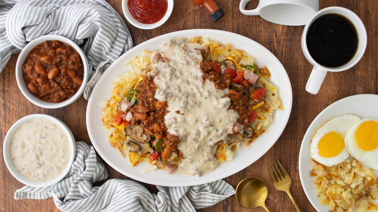 Plate of Copycat Waffle House All-the-Way Hash Browns on serving platter next to bowls of with chili and gravy