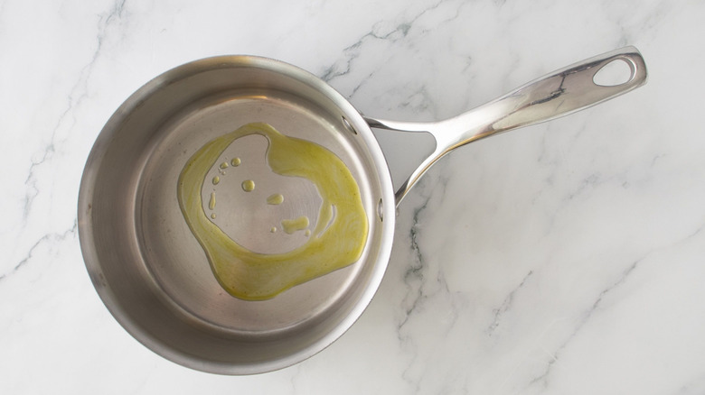 Olive oil drizzled in stainless steel saucepan on marble surface