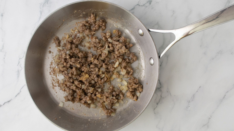 Cooked sausage and onions in skillet on marble surface