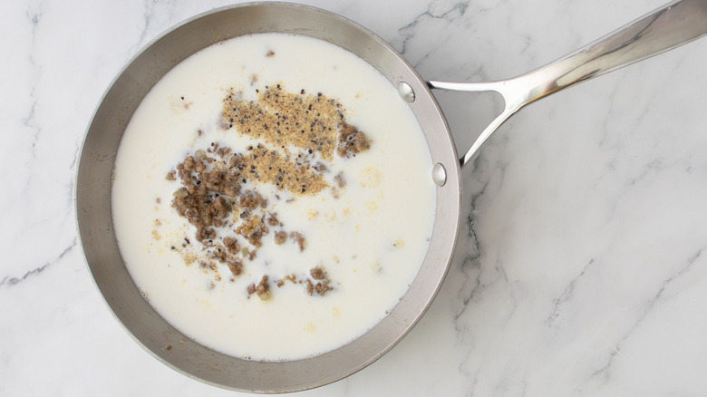 Milk, sausage, and seasoning in skillet on marble surface