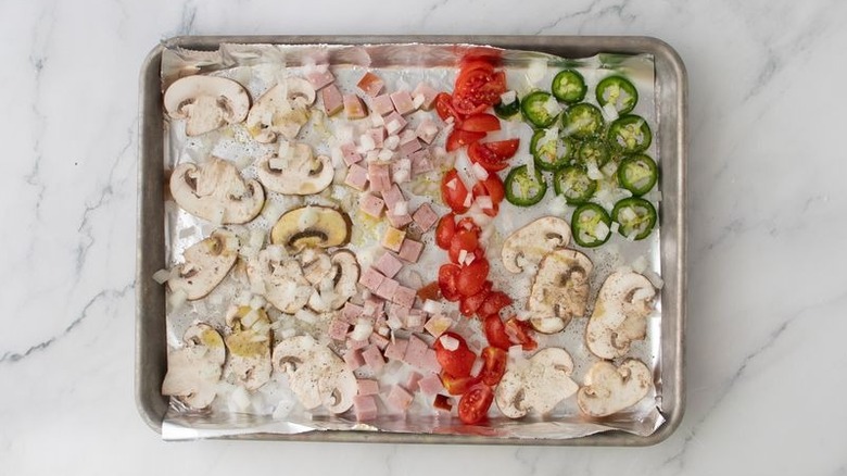 Various vegetables and ham spread out on foil-lined baking sheet