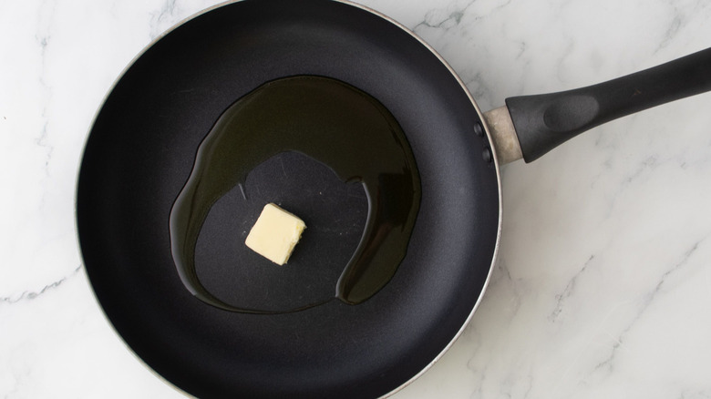 Olive oil and pat of butter in skillet on marble surface