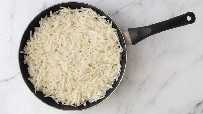 Uncooked hash browns spread out in a skillet on marble surface