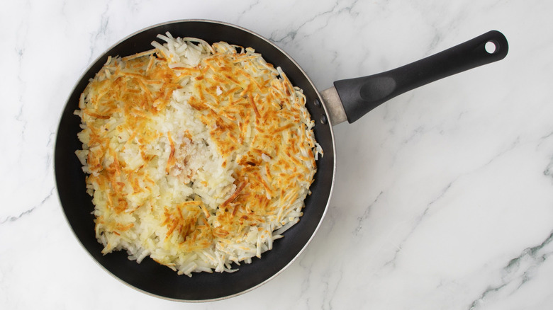 Browned hash browns in a skillet on marble surface