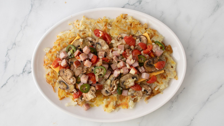 Platter of hash browns topped with grilled veggies and ham