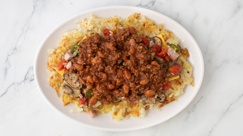 Platter of hash browns with grilled veggies and chili on marble surface