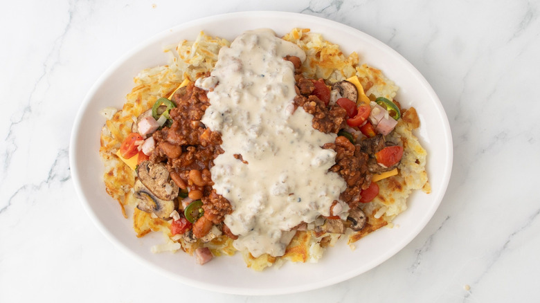 Platter of hash browns with grilled veggies, chili, and gravy on marble surface