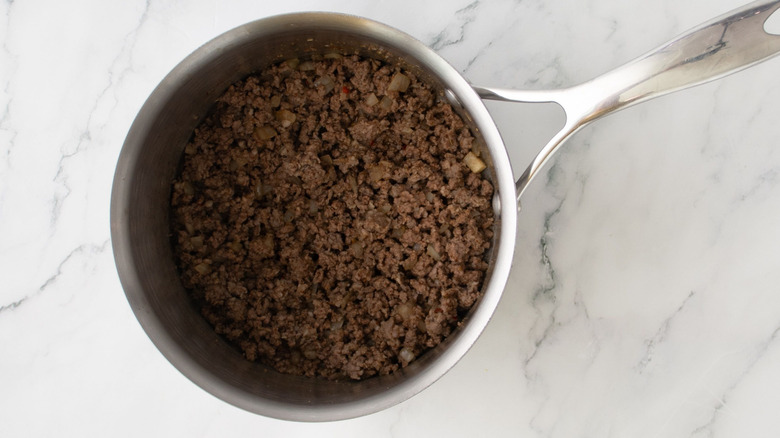 Cooked ground beef and sausage in saucepan on marble surface