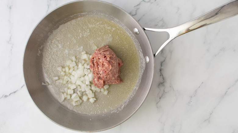 Melted butter, diced onion, and raw sausage in a stainless steel skillet