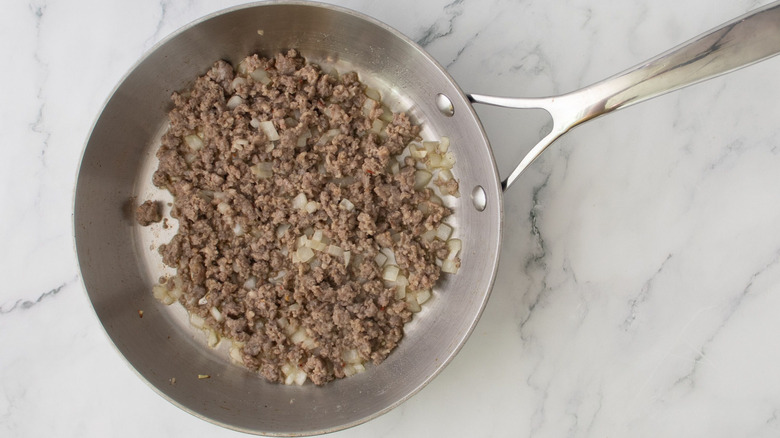 Cooked ground sausage and onions in skillet on marble surface