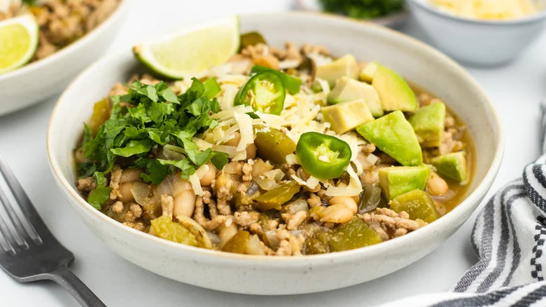 Bowl of ground pork chili with peppers, avocado, lime, and cilantro as toppings