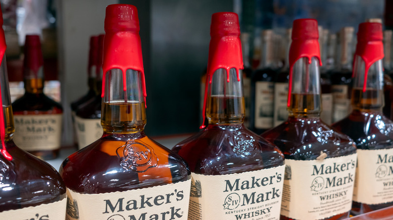 Row of Maker's Mark whisky bottles lined up on store shelf.