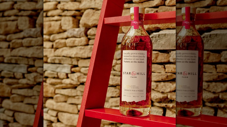 Bottle of Star Hill Farm Whisky on red wooden ladder against a stone wall.