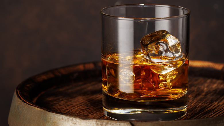 A glass of bourbon with ice on a dark wooden barrel