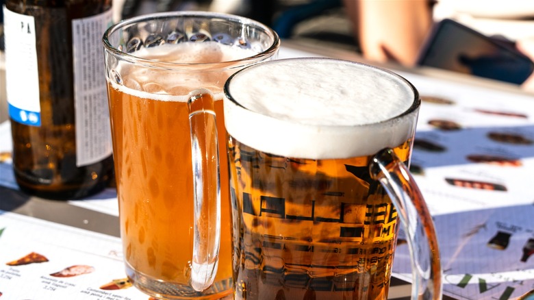Glass mug of malt liquor next to mug of beer.