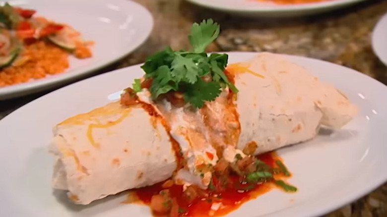 A burrito topped with a red sauce and a green cilantro leaf on a white plate at Mama Rita's restaurant