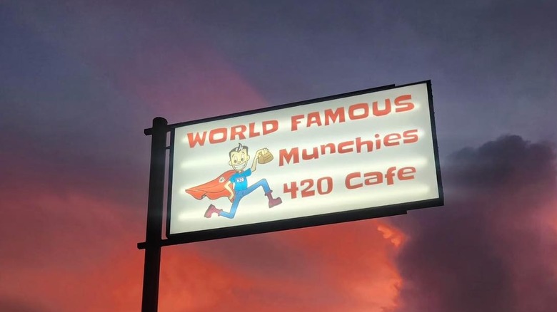 World Famous Munchies 420 Cafe sign on pole featuring cartoon of thin superhero, sunset in the background