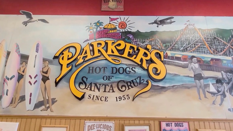 Mural inside Parker's Hot Dogs of Santa Cruz restaurant with restaurant's name over a beach with surfers, children playing, and a roller coaster
