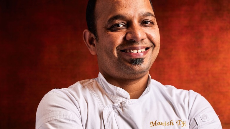 Chef Manish Tyagi smiling against red backdrop