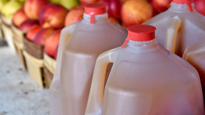 Gallons of apple cider sit in front of baskets of green and red apples.