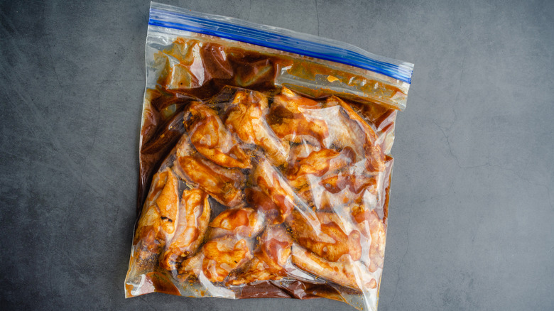 A zip-top bag full of sauce and raw chicken sits on a plain concrete background.
