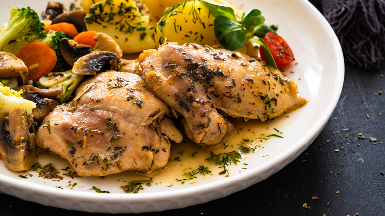 Chicken thighs on white plate with veggies atop black table
