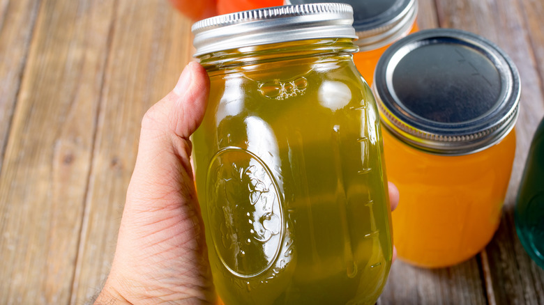 Hand holding jar of pickle juice with other jars of different liquids in other colors on wooden table