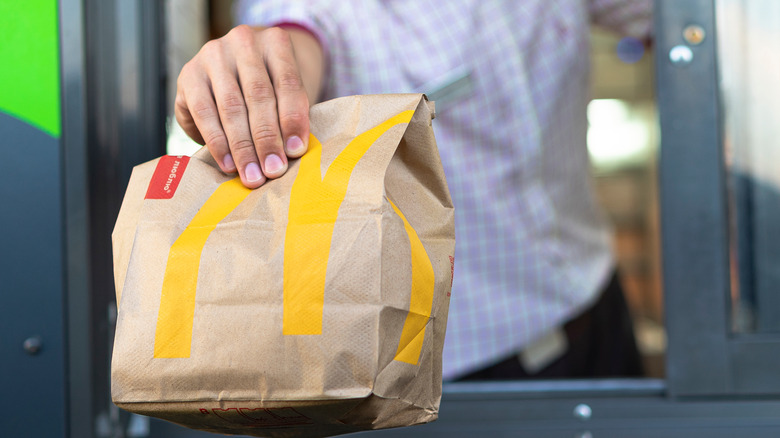 A McDonald's employee handing a bag of food to a customer at the drive-thru.