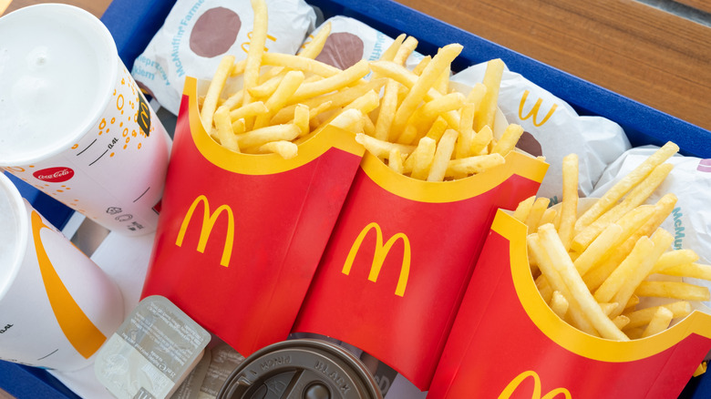 Three cartons of McDonald's french fries on tray with drinks, sandwiches, and sauces