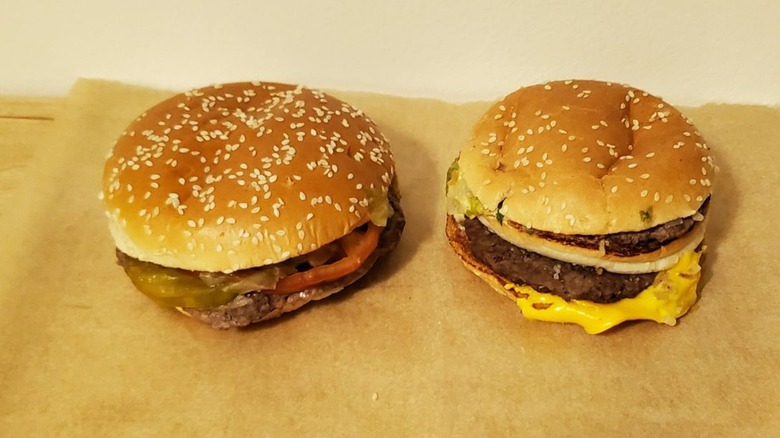 Burger King Whopper with tomato and pickle next to McDonald's Big Mac with cheese, both with sesame seed buns, on brown paper