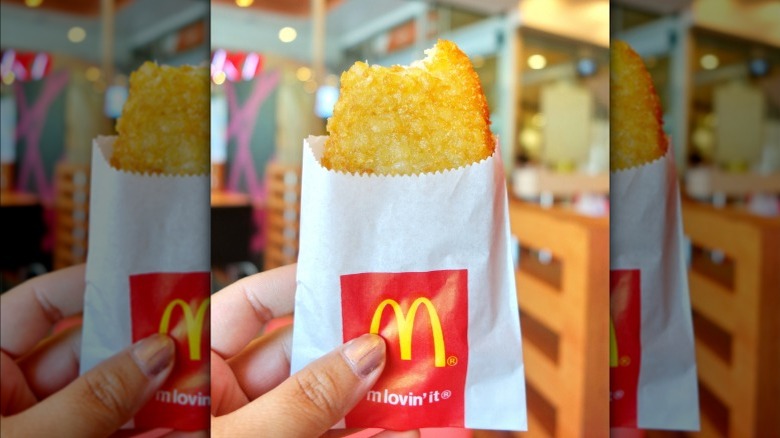 Hand holding up McDonald's hash brown in paper sleeve.