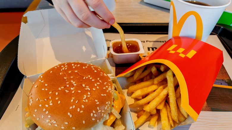 Dipping a fry into sauce near burger and drink.