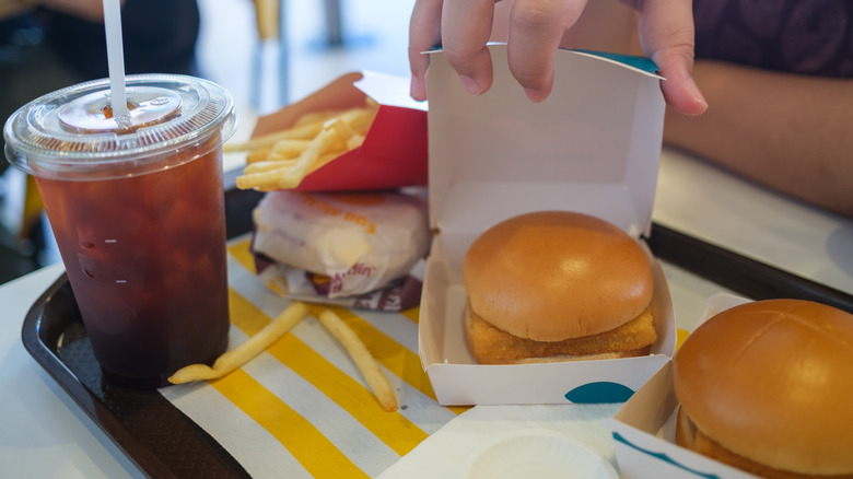 Hand opening a McDonald's Filet-O-Fish box on tray with other menu items.