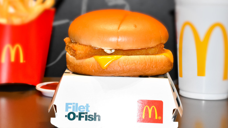 A McDonald's Filet-O-Fish sandwich sits atop its box with fries and a drink in the background.