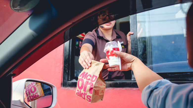 McDonald's employee handing customer a bag of food and ice cream cup in drive-thru