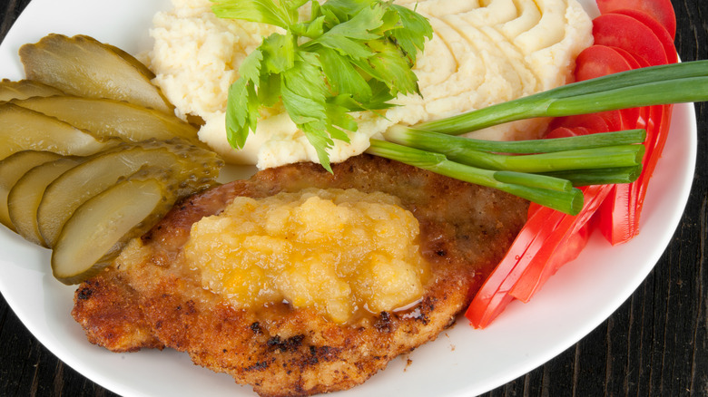 Close-up of pork chops with applesauce, mashed potatoes and pickles