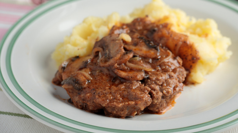 Salisbury steak with mushrooms and mashed potatoes on white plate