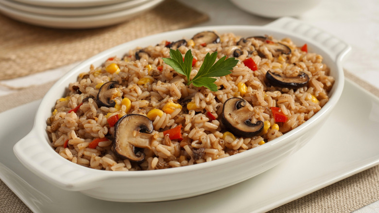 Rice and mushroom casserole in a white serving dish garnished with a parsley sprig