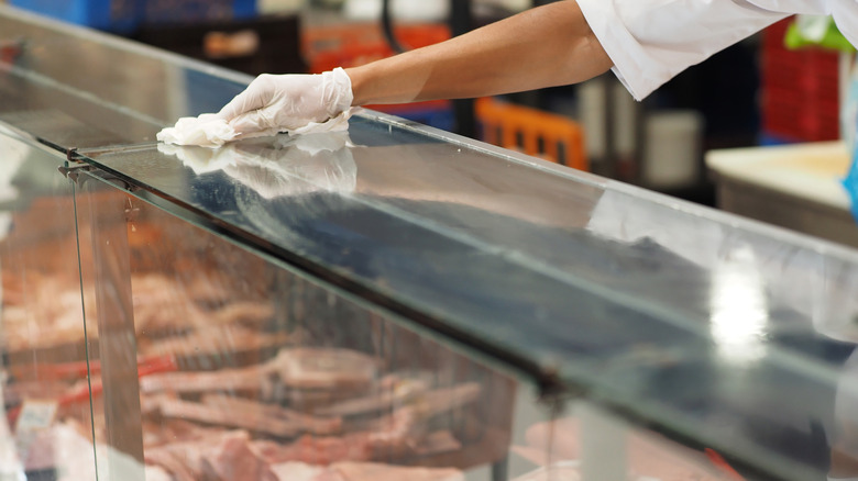 Employee cleaning supermarket meat counter