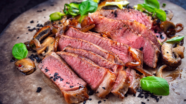 Sliced beefsteak displayed on stone plate with mushrooms, onions, and garnishes.
