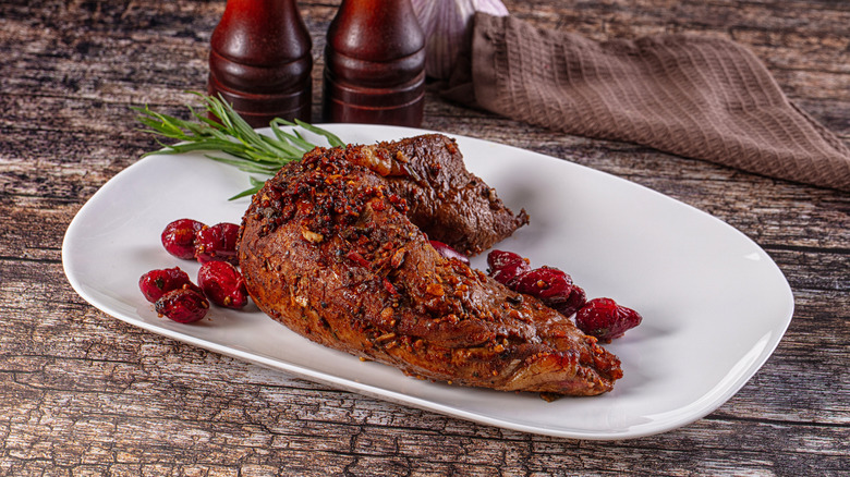 Baked pork sirloin and garnishes on white plate.