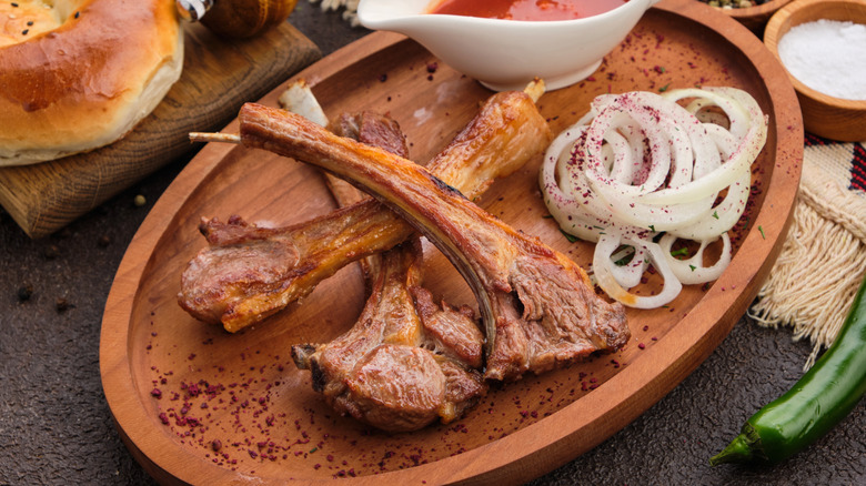 Grilled veal loin on wooden tray with sauce, onions, and bread.