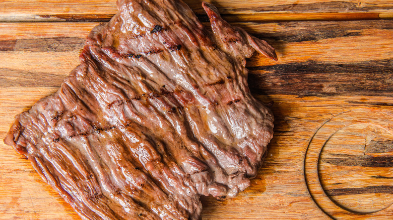 A grilled flank steak resting on a wooden cutting board