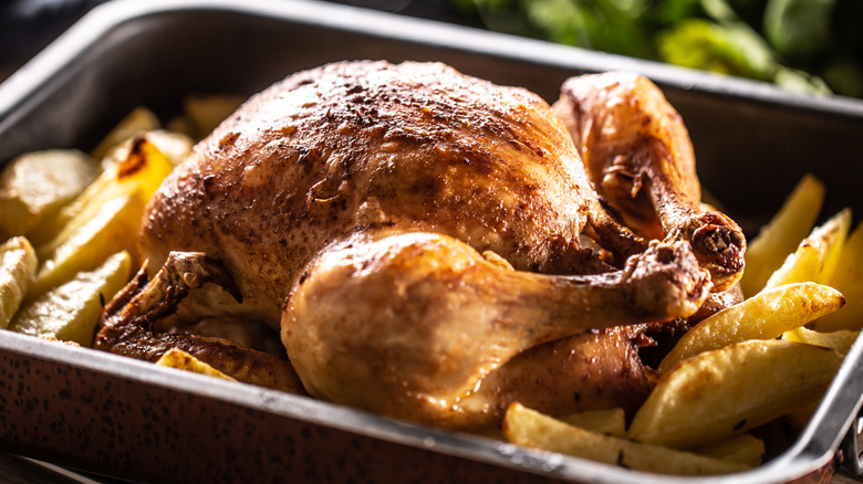 Whole roast chicken in pan with potato wedges