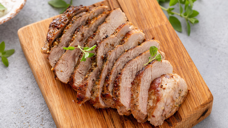 Sliced pork chop with garnish on wooden cutting board