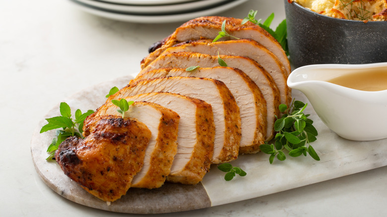 Sliced turkey breast on marble cutting board with gravy boat
