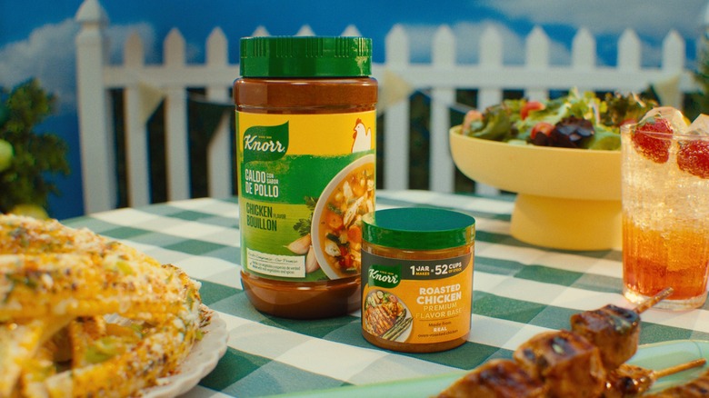 Jars of Knorr chicken seasoning on picnic table in an artificial backyard set.