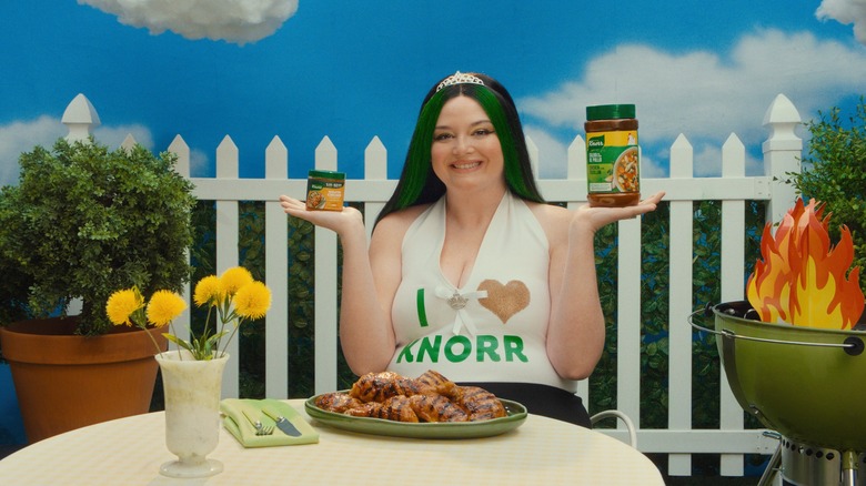 Meg Stalter posing with Knorr seasoning products, a plate of grilled chicken on the table in front of her.