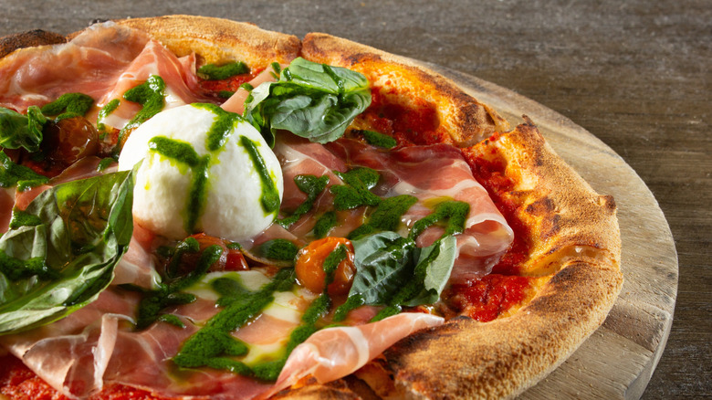 Pizza with burrata cheese, basil, pesto, and prosciutto