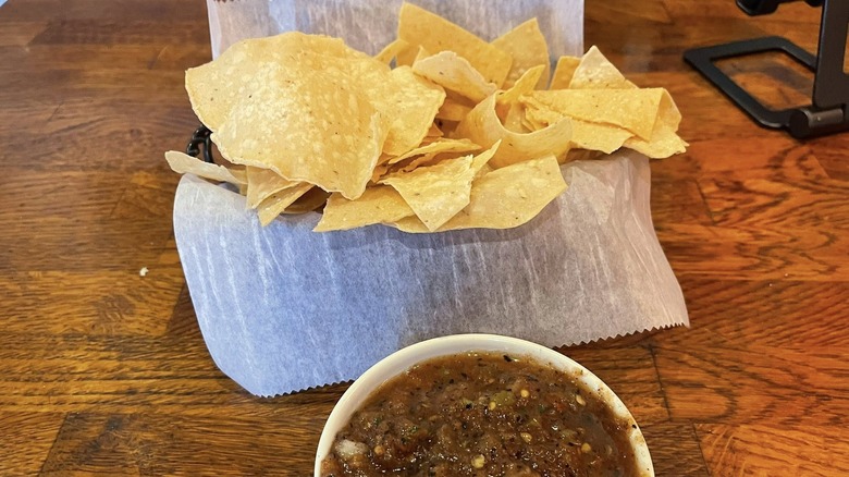 A basket of chips and bowl of salsa on a wooden table